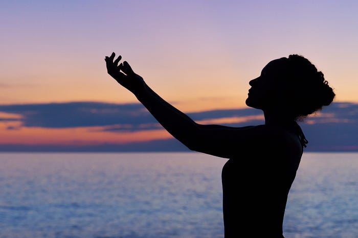 Dark figure of a woman in silhouette against a sky and seascape.